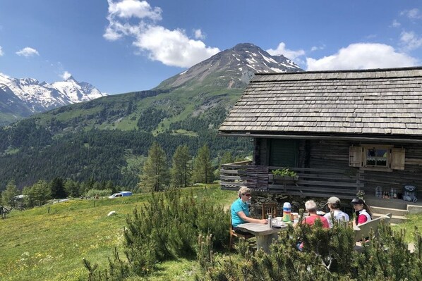 Una cabaña de madera con una mesa y sillas en el exterior, rodeada por un paisaje montañoso.