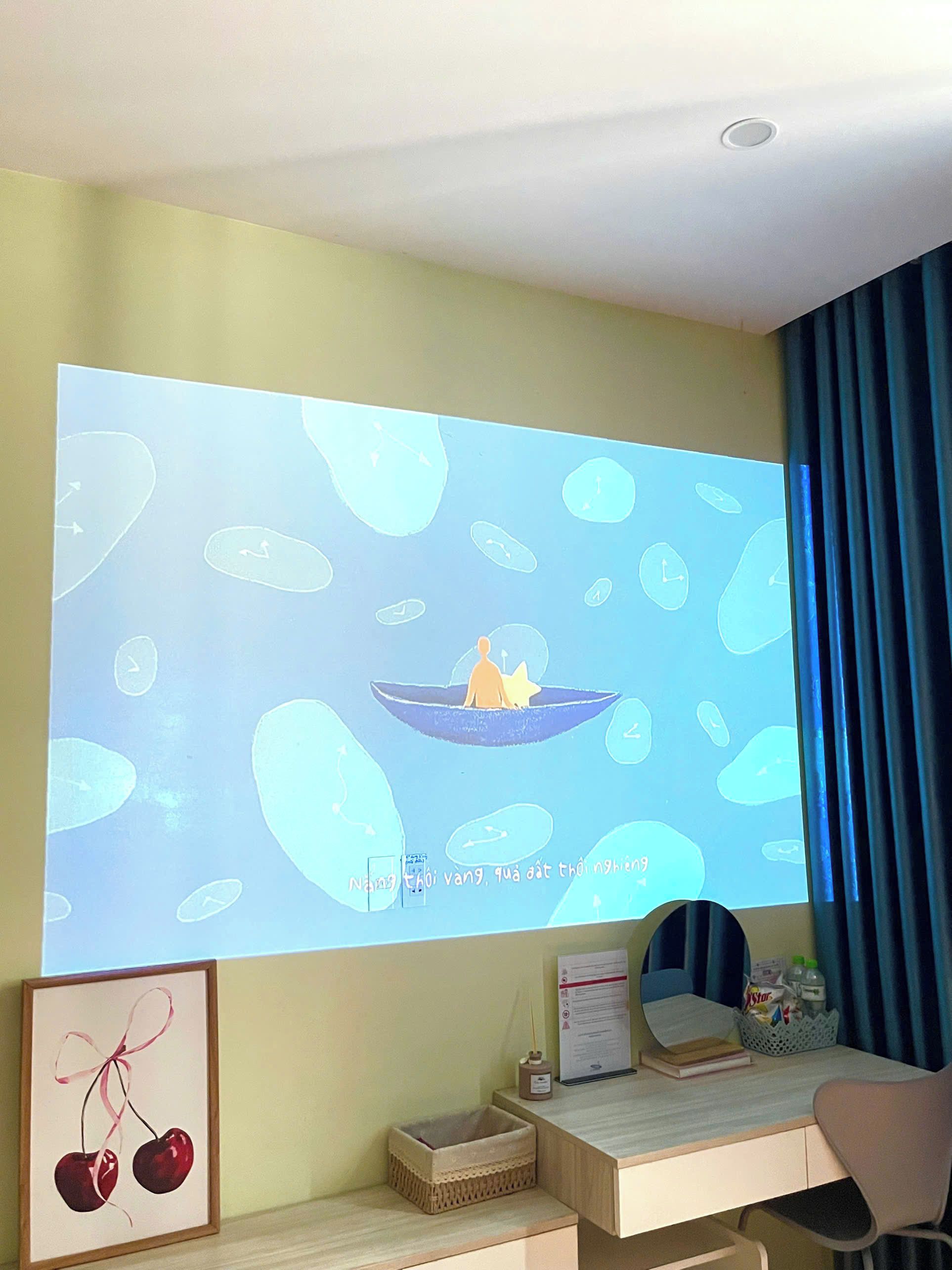 Ein Zimmer mit einer Projektionsleinwand, die eine Präsentation zeigt, einem Schreibtisch mit Stuhl, einem gerahmten Bild und einem Korb mit Gegenständen.