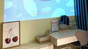 Una habitación con una pantalla de proyección mostrando una presentación, un escritorio con una silla, un cuadro enmarcado y una cesta con objetos.