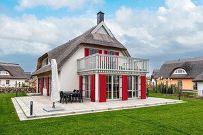 Ein Haus mit einem Strohdach, einem Balkon mit roten Fensterläden und einem gepflegten Rasen.