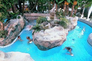 Ein Schwimmbecken mit Wasserfall, umgeben von tropischer Vegetation und Felsen.