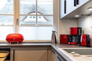 A kitchen with a window, a red kettle, a red coffee maker, and a red appliance on the counter. - Holiday home with 4 bedrooms (18445 Kramerhof, Deutschland)