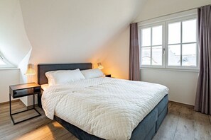 Ein ordentlich eingerichtetes Schlafzimmer mit einem Bett, Nachttischen und einem Fenster mit Vorhängen.