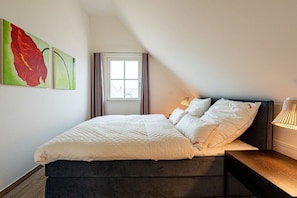 A bedroom with a bed, a nightstand, a lamp, and two wall-mounted paintings. - Holiday home with 4 bedrooms (18445 Kramerhof, Deutschland)