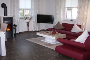 Ein modernes Wohnzimmer mit Kamin, Flachbildfernseher, einem roten Sofa und einem Couchtisch.