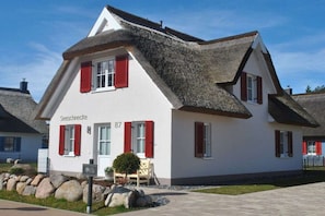 Ein traditionelles Haus mit einem steilen Satteldach, roten Fensterläden und einer kleinen Veranda.