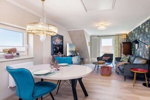 A modern living room with a dining area, a chandelier, and a sofa with cushions. - Holiday apartment with 1 bedroom (Saßnitz)