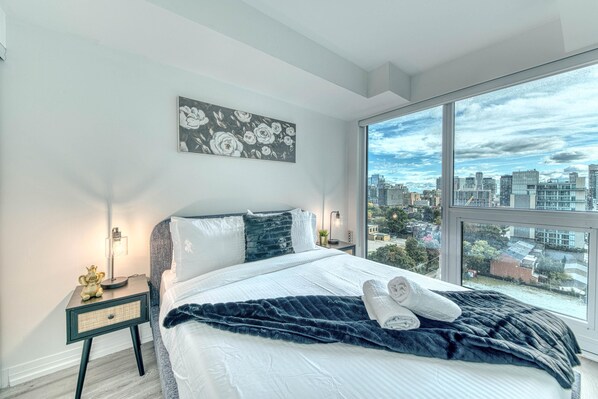Un dormitorio moderno con una cama grande, vistas a la ciudad y un cuadro en la pared.