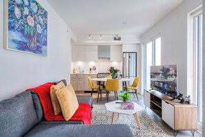 Una sala de estar moderna con un sofá gris, cojines rojos y beiges, una pequeña mesa de centro con una planta y un televisor sobre un mueble de madera.