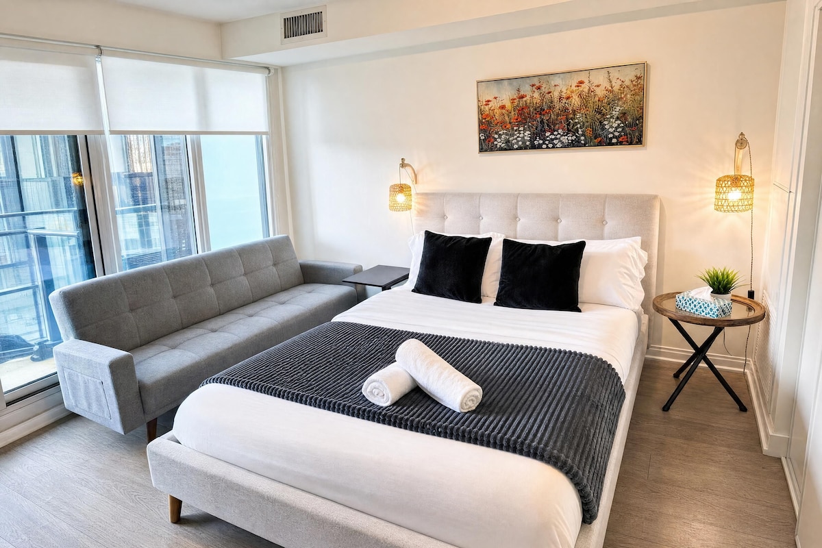 Un dormitorio moderno con una cama grande, un sofá gris y una pequeña mesa con una planta.