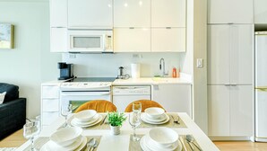 A modern kitchen with white cabinets, a microwave, a stove, and a dishwasher. There is a dining table set with plates, glasses, and cutlery. - StayToronto - Terrace 21 Apartments (Toronto)
