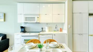 A modern kitchen with white cabinets, a microwave, a stove, and a dishwasher. There is a dining table set with plates, glasses, and cutlery.