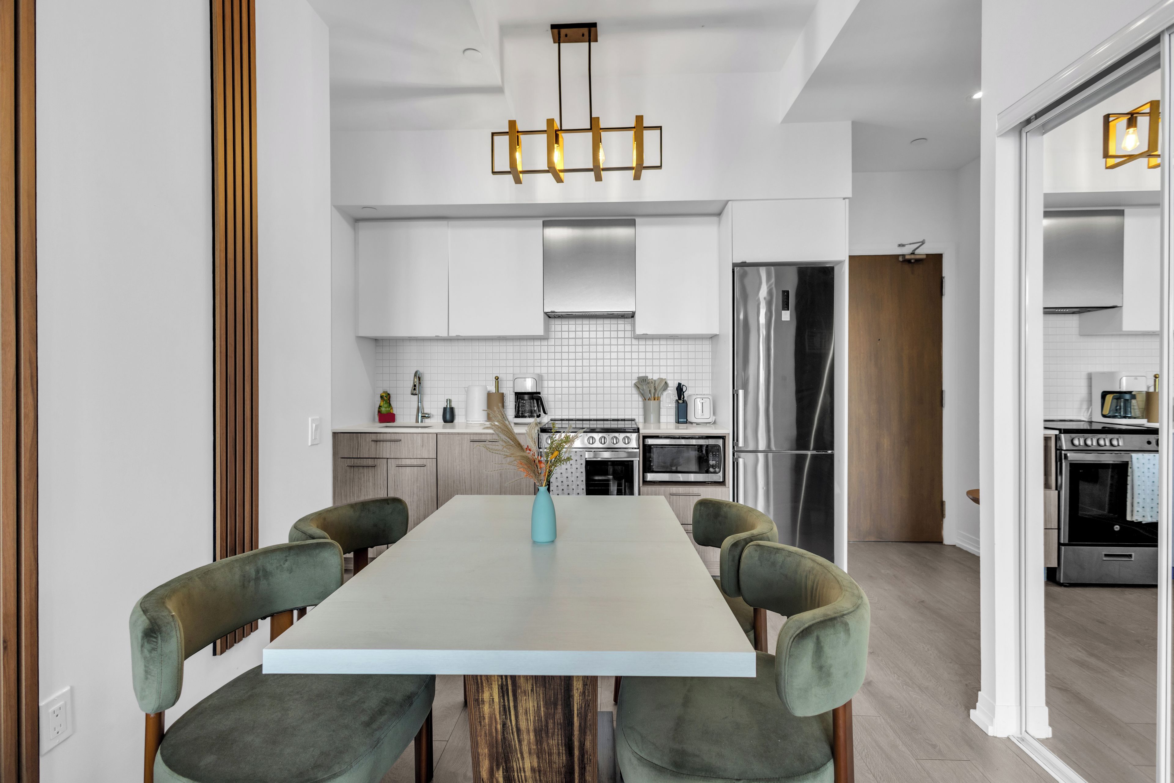 A modern kitchen with white cabinetry, a central island, and a dining area with green upholstered chairs.