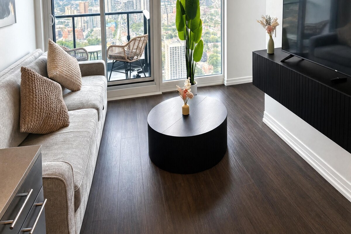 Una sala de estar moderna con un sofá, una mesa de centro, un televisor y un amplio ventanal con vista a la ciudad.