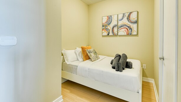 A small, single-bed room with a wooden floor, a white bed, and a wall-mounted abstract art piece. - StayToronto - Terrace 21 Apartments (Toronto)