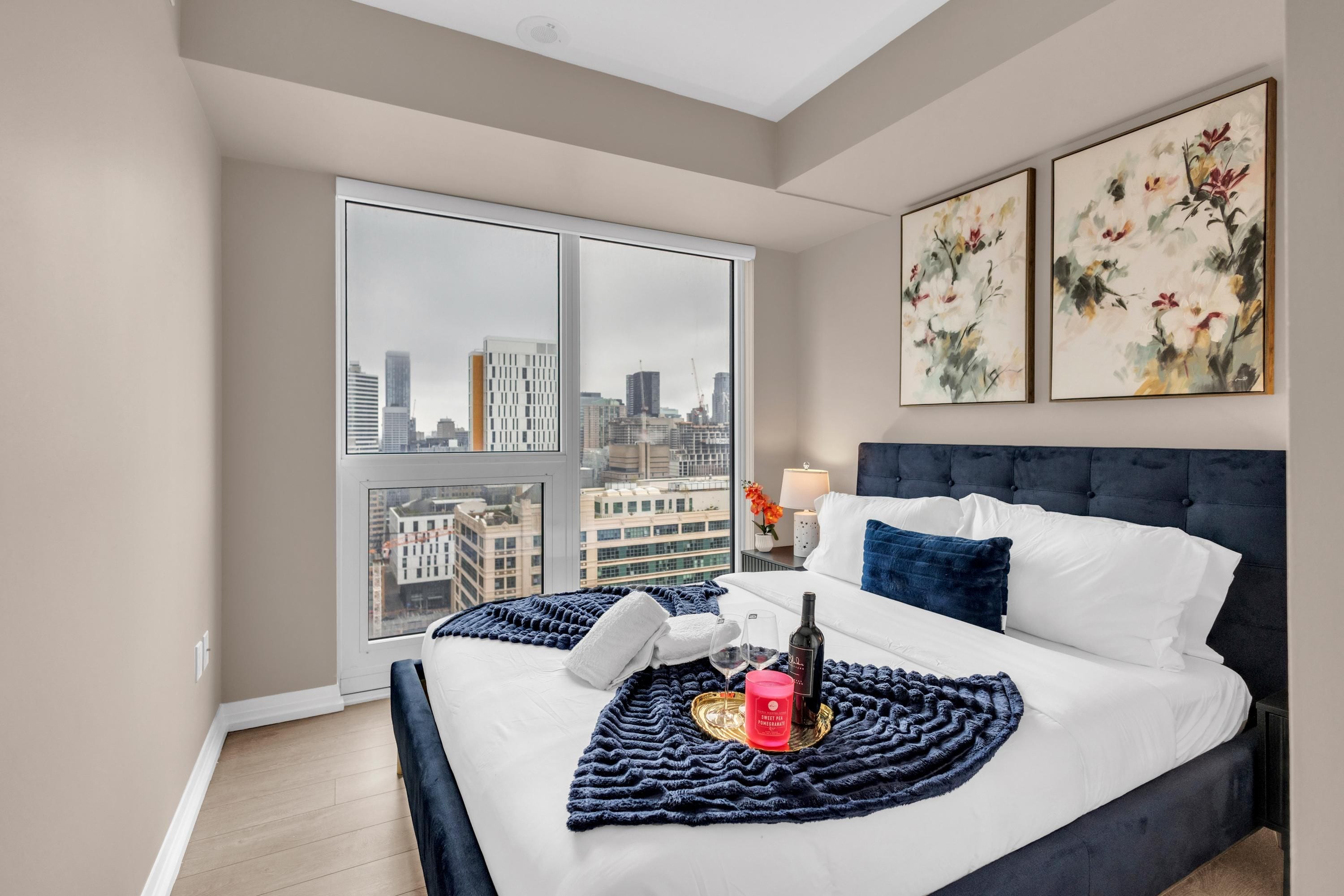 A hotel room with a large bed, a city view, and two floral paintings on the wall.