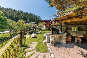 Ein rustikaler Außenbereich mit einem Stein-Barbecue, Holzbanken und einem Steinweg, der zu einem Haus mit Gründach führt.