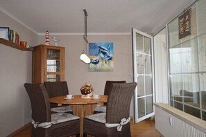 Uma sala de jantar com mesa e cadeiras de madeira, um quadro na parede e uma janela com vista.