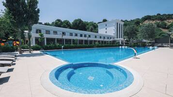 Une piscine avec une terrasse carrelée, une aire de jeux pour enfants et un bâtiment doté de nombreuses fenêtres en arrière-plan.