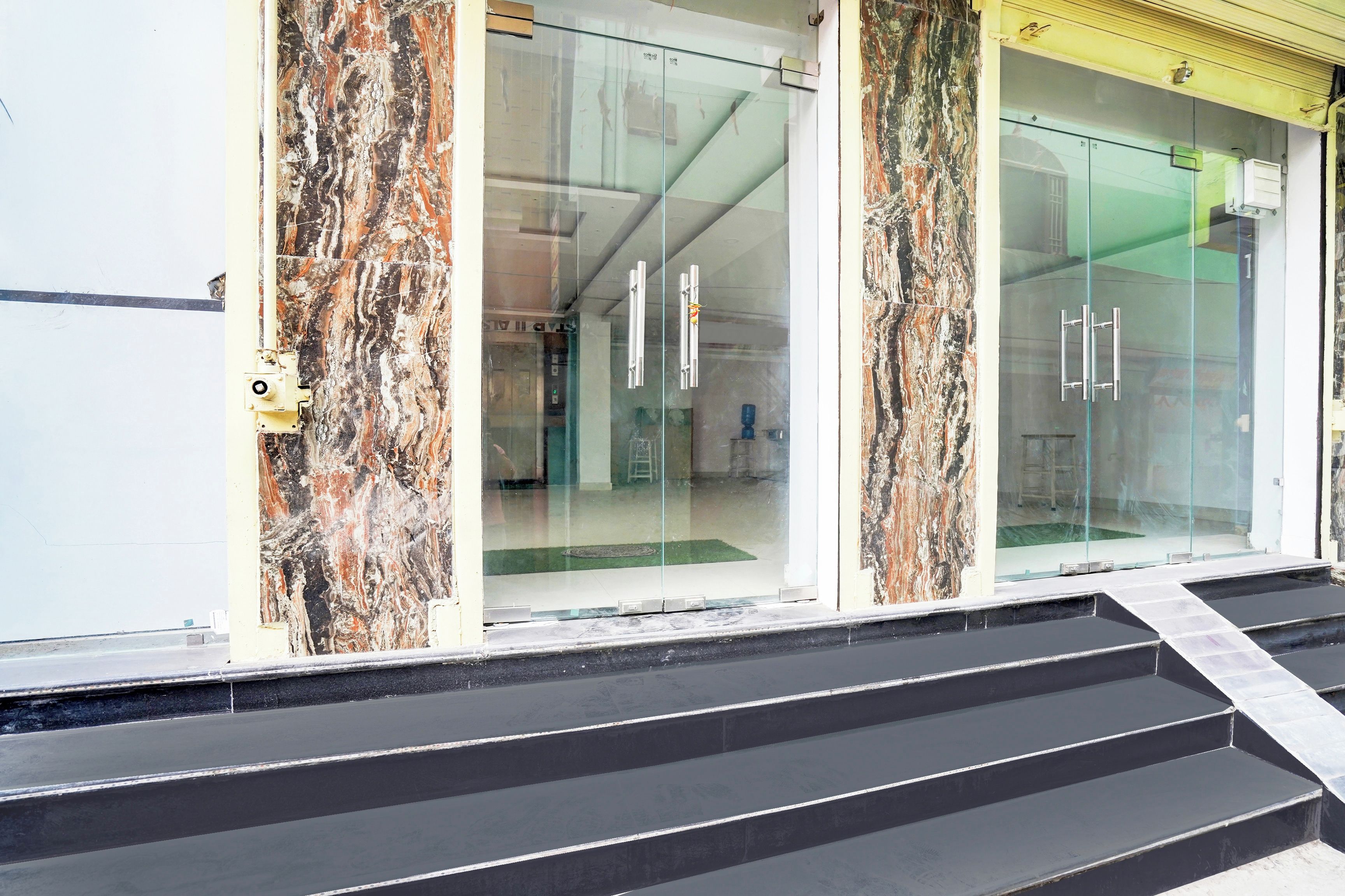 A building entrance with a glass door, a marble facade, and a set of stairs leading up to the entrance.