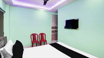 Un dormitorio con una cama, dos sillas rojas, un televisor en la pared y un ventilador de techo.