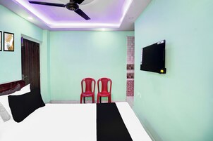 A bedroom with a bed, a ceiling fan, a TV mounted on the wall, and two red chairs.