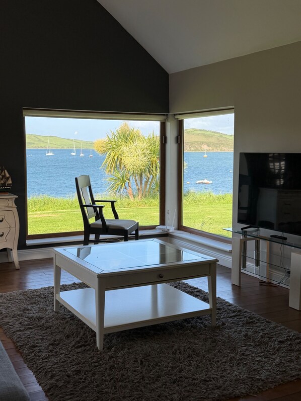 A modern living room with a large window overlooking a body of water and sailboats.