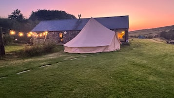 A grassy field with a tent and a building with a sloped roof.