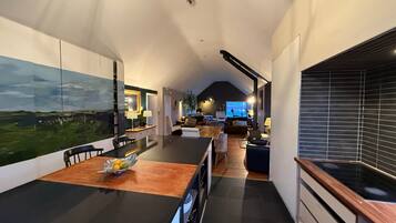 A modern kitchen with a large island, a dining area with a table and chairs, and a living space with a sofa and a TV.