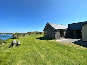 A stone house with a sloped roof, a grassy yard, and a view of the sea.