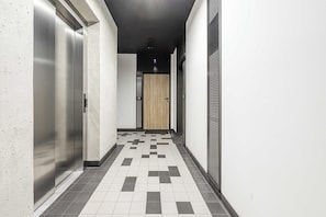 Ein Korridor mit einem Schachbrettmuster auf dem Boden, einer Tür am Ende und einer Wand mit einer strukturierten Oberfläche.