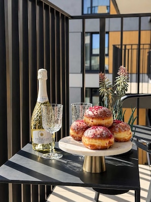 Eine Flasche Prosecco, zwei Gläser und ein Tablett mit drei Donuts auf einem Tisch im Freien.