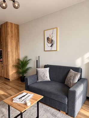 Un salon moderne avec un canapé gris, un meuble en bois, une plante en pot et une œuvre d’art abstraite encadrée accrochée au mur.