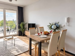 Un coin repas avec une table dressée pour six personnes, un téléviseur, une plante en pot et une vue sur l’extérieur.