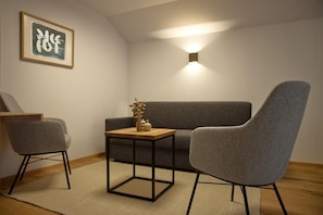 A modern living room with a grey sofa, a grey armchair, a small wooden table with decorative items, and a framed artwork on the wall. - Modern suite with garden or loggia (Gaschurn)