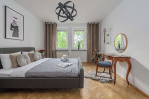 Ein Schlafzimmer mit Bett, Schreibtisch, Stuhl, Spiegel und einem Fenster mit Vorhängen.