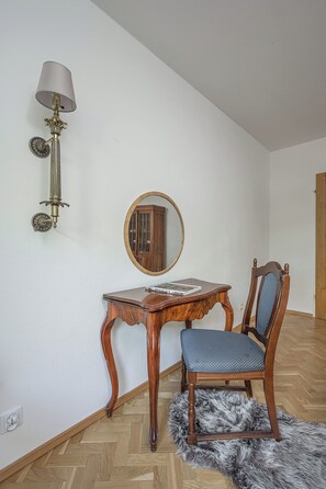 Ein Zimmer mit einem Holztisch, einem Stuhl, einem Spiegel und einer Wandlampe.