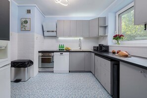 Une cuisine moderne avec des meubles blancs, un lave-vaisselle, un évier et une fenêtre donnant sur les arbres.