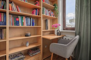 Ett studierum med trähyllor för böcker, ett skrivbord, en stol och ett fönster med utsikt över byggnader.