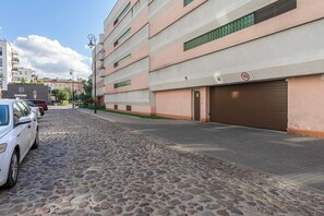 En gata med kullerstenar, en parkerad vit bil och en byggnad med flera fönster och en garageport.