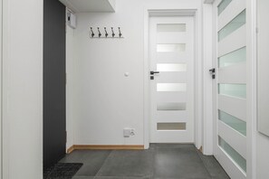 Ein Flur mit einer weißen Tür mit Milchglasfenstern, einem Kleiderhaken mit fünf Haken und einer kleinen Steckdose an der Wand.
