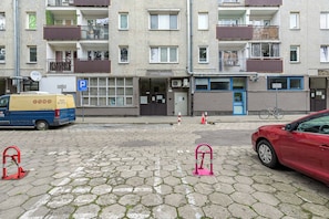 En flervåningsbyggnad med bostäder och balkonger, en parkeringsskylt och en leveransbil parkerad på gatan.