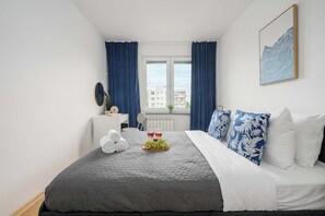 A bedroom with a bed, a bedside table, a window with curtains, and a wall-mounted picture. - Lumina 3-room Apart w/ Balcony near Arkadia Mall (Warszawa)
