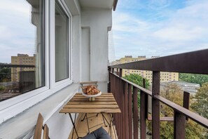 A balcony with a wooden table and a plate of croissants, overlooking a cityscape. - Lumina 3-room Apart w/ Balcony near Arkadia Mall (Warszawa)