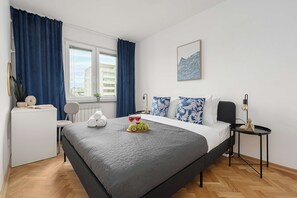 Ein modernes Hotelzimmer mit einem großen Bett, einem Nachttisch, einem Sessel, einem Fenster mit Vorhängen und einem Wandbild.