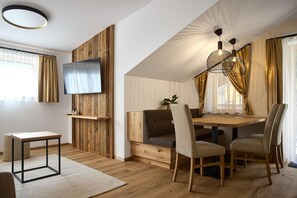 A modern interior with a wooden wall-mounted TV, a dining area with a wooden table and chairs, and a ceiling light fixture. - Modern suite with outdoor sauna (Gaschurn)
