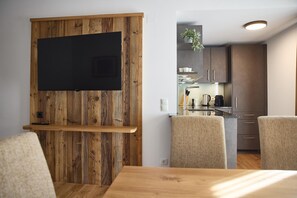 A modern kitchen with a built-in stove, cabinets, and a dining area with a wooden table and chairs. - Penthouse suite with outdoor sauna (Gaschurn)