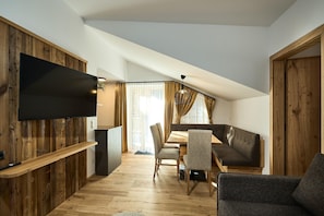 A modern living space with a flat-screen TV mounted on a wooden wall, a dining area with a table and chairs, and a cozy seating area with a sofa and armchairs. - Penthouse suite with outdoor sauna (Gaschurn)