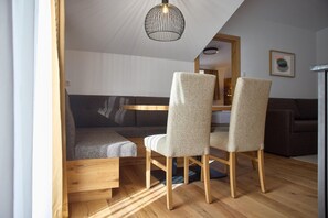 A room with a wooden dining table, two chairs, a sofa, and a hanging light fixture. - Penthouse suite with outdoor sauna (Gaschurn)