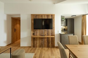 Un saló modern amb una paret d'accent de fusta, una televisió de pantalla plana, una zona de menjador amb taula i cadires de fusta, i una cuina al fons.